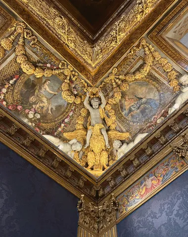 Ornate gilded ceiling corner at the Musée Carnavalet, with a carved figure and painted panels above blue wall hangings