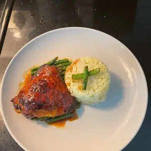 Glazed chicken thigh with rice and green beans on a white plate